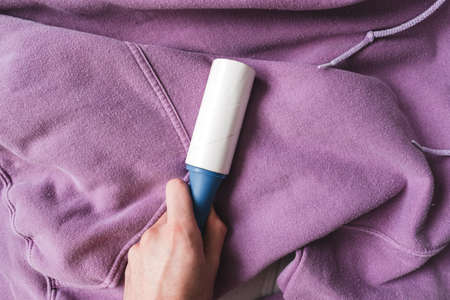 Hands holding blue sticky roller for cleaning clothes. High quality photo