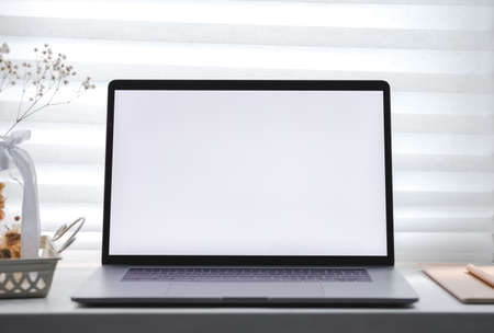 A laptop with a white blank screen and a notebook on the window on a sunny day. Workplace home, mock up. High quality photoの写真素材
