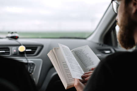 Young bearded caucasian man reads a book in a car during a long trip. High quality photo