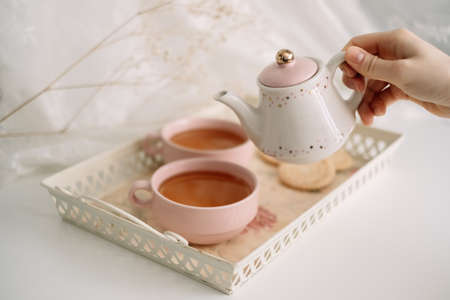 A woman pours tea from a teapot into a pink cup. Breakfast at home. High quality photoの写真素材