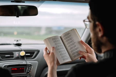 Young bearded caucasian man reads a book in a car during a long trip. High quality photoの写真素材