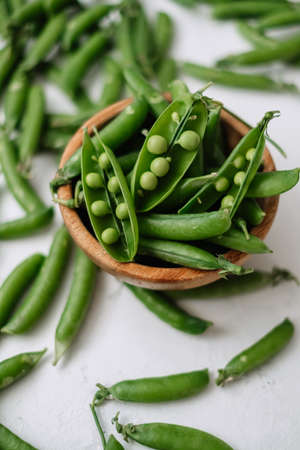 Green fresh peas in a wooden bowl on a white table. High quality photoの写真素材