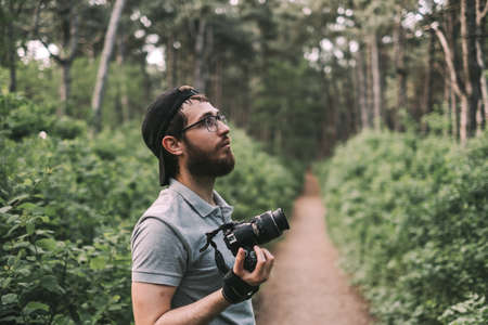 Young man tourist takes pictures on a camera in a forest. Tourism, active lifestyle. High quality photoの写真素材
