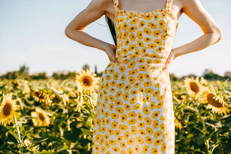 Young caucasian woman in sunflower dress standing in sunflower field on a sunny day. High quality photoの写真素材