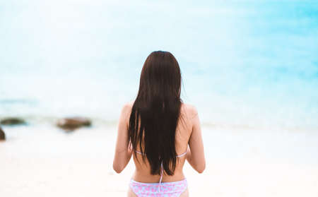 A young caucasian woman in swimsuit stands on a beach with blue water and white sand. swimming...