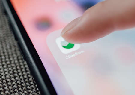 Russian bank Sberbank, iPhone with icon of Sberbank Online app and finger tap.