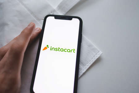 Instacart app logo on the smartphone screen with white shop eco bag.
