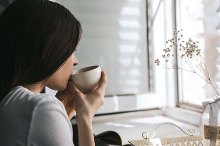 Woman drinking tea sitting by the window on a sunny spring morning.
