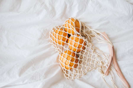 Mesh eco bag with fresh oranges on a white cloth at home. Top view.の写真素材