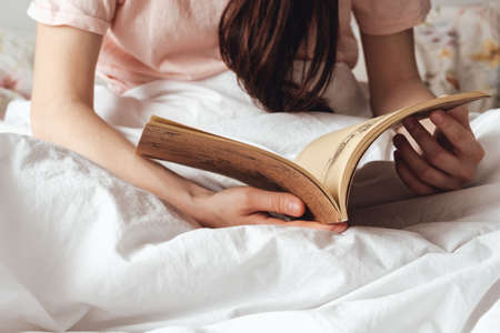 Woman holds open book in hands, lying in bed at home. Home reading concept