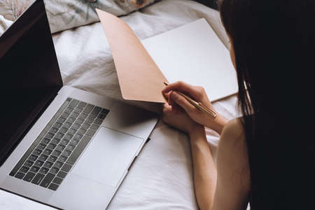 Young woman lies on bed with laptop and notebook. Distance education, remote work.の写真素材