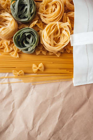 Varieties of Italian pasta. White eco bag with spaghetti, farfalle and tagliatelle on a craft paper background. Non-perishable food.の写真素材