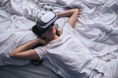Woman uses virtual reality glasses at home on the bed. Plays games, technologies of the future.の写真素材