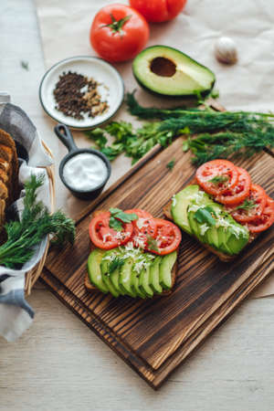 Healthy vegan homemade sandwich, avocado and tomatoes with dark grain bread on a wooden board.の写真素材