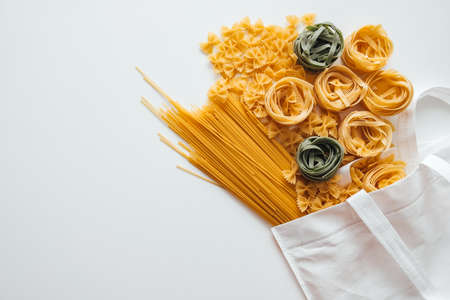 Varieties of Italian pasta. White eco bag with spaghetti, farfalle and tagliatelle on a white background. Non-perishable food.の写真素材