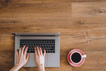 Female hands are typing on laptop keyboard. Wooden background with a cup of coffee.の写真素材