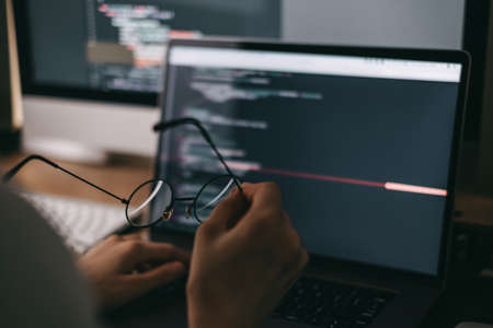 Young caucasian female programmer in glasses writes program code on a laptop computer. home office. High quality photoの写真素材