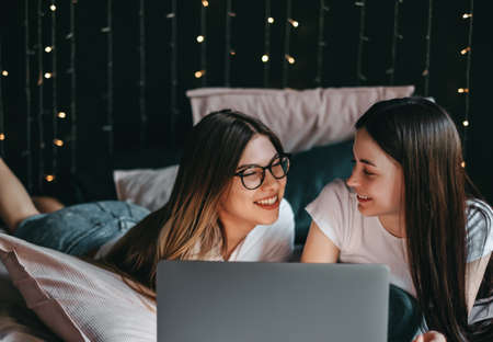 Young beautiful caucasian women's lesbian couple lover, using laptop computer, shopping online together in living room at home in the bed. Concept of LGBT sexuality. High quality photoの写真素材
