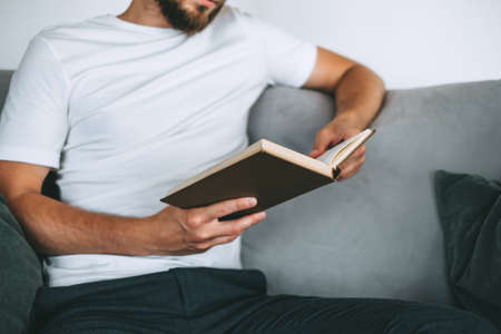 Young caucasian man resting on a sofa and reading a book. Home leisure. High quality photoの写真素材