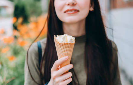 Young pretty woman eating ice cream in a waffle cone while walking along the street in the park alone. High quality photoの写真素材