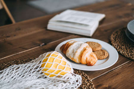 Book and croissant with cookies on a wooden kitchen table. Domestic life. High quality photo