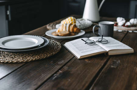 Wooden kitchen table with breakfast, book, cup of coffee and growing. High quality photoの写真素材