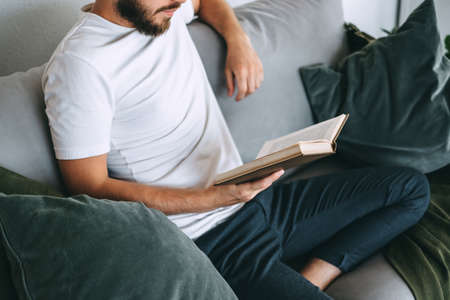 Young caucasian man resting on a sofa and reading a book. Home leisure. High quality photoの写真素材