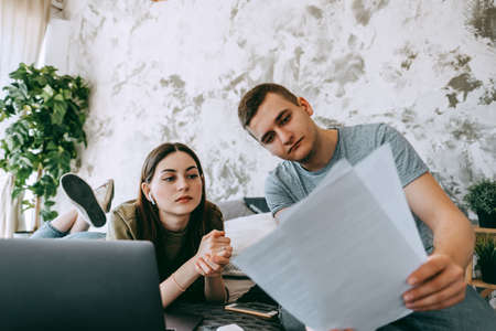 Coworkers discussing project and using laptop together, watching paper documents. Business colleagues together in cozy office space. Partnership or consulting concept. High quality photoの写真素材