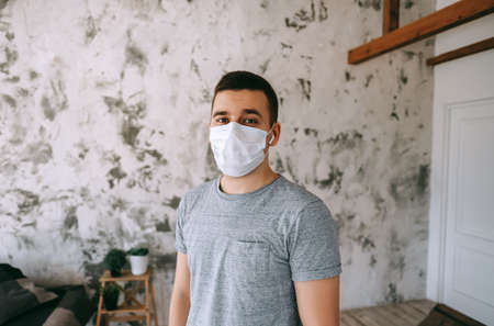 Portrait of Young brunette white European man at home on quarantine with medical mask in living room.の写真素材