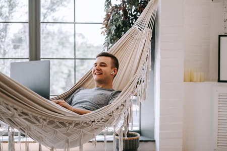 Young caucasian freelancer in headphones works on a laptop, browses the internet while lying in a...