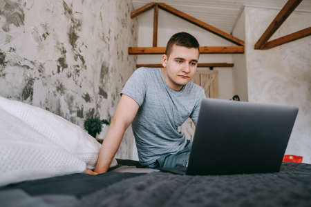 A young caucasian man using laptop, browses the internet while sitting in sofa at the home. A person working on electronic devices.の写真素材