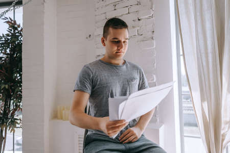 Young man sitting on a chair and looking at paper documents bills.