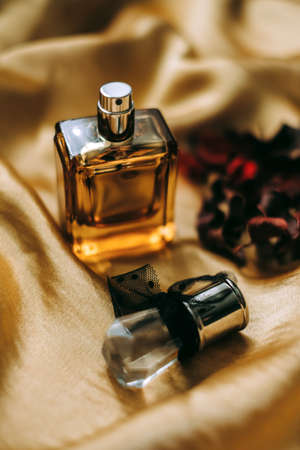Perfume bottle on golden satin fabric with dried flower petals, close-up, warm light. ... High...