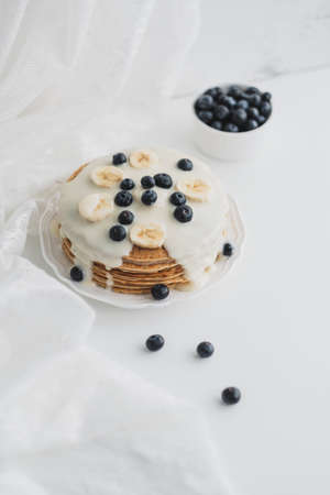 Pancakes with condensed milk with fresh blueberries and banana in a white plate on a white...