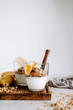 Muesli and natural yogurt with slices of fruits and nuts in a glass cup on a wooden board, healthy...
