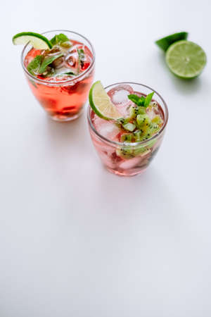 Raspberry cocktail, lemonade with lime, kiwi, mint and pieces of ice on a white table.の写真素材