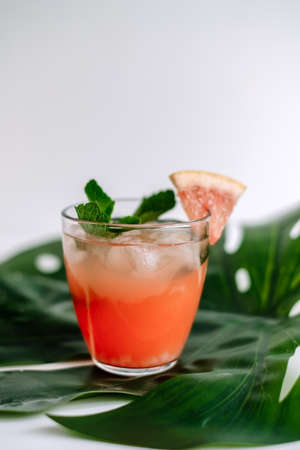 Grapefruit cocktail, lemonade with lime, mint and ice cubes on a green tropical leaf.の写真素材
