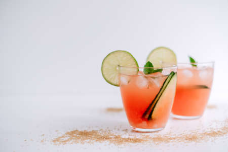 Grapefruit cocktail, lemonade with lime, mint and pieces of ice on a white table with cane sugar.の写真素材