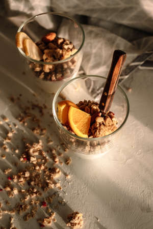 Granola and natural yogurt with slices of fruits and nuts in a glass cup. Warm sunlight with shadow, healthy breakfast.の写真素材