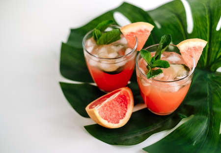 Grapefruit cocktail, lemonade with lime, mint and ice cubes on a green tropical leaf. High quality photoの写真素材