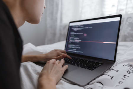 Young female programmer writes program code on a computer laptop in the bed at home. remote work. High quality photoの写真素材