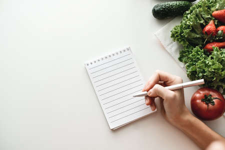 Woman makes notes in a notebook, food shopping list or writing recipes. Mock up. High quality photoの写真素材