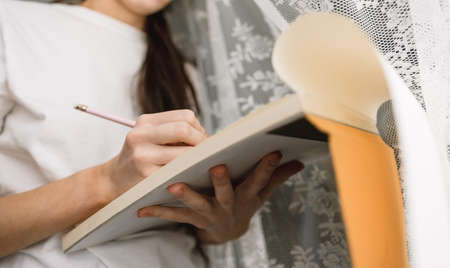 Woman draws in a sketchbook at home near the window, creativity. Drawing training. High quality photoの写真素材