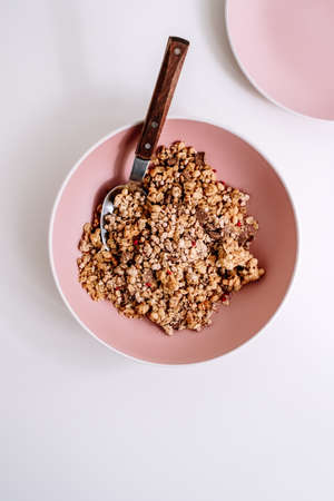 Granola muesli with pieces of chocolate in a pink plate on a white table. Healthly food, breakfast concept. High quality photoの写真素材