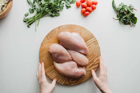 Chicken fillet on a wooden board with herbs, white background. Cooking preparation. Flat lay. High...