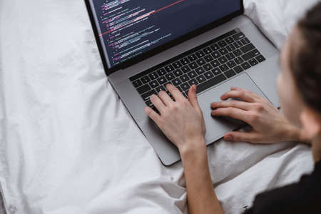 Young female programmer writes program code on a computer laptop in the bed at home. remote work. High quality photoの写真素材