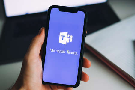 Hand holding iPhone with Microsoft Teams video call app logo on the screen. High quality photoのeditorial素材
