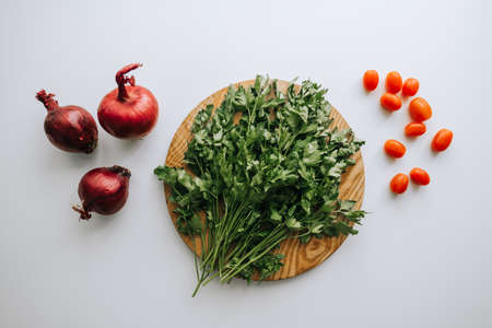 Green parsley on a wooden board, red onion and cherry tomatoes, white background. Proper nutrition....