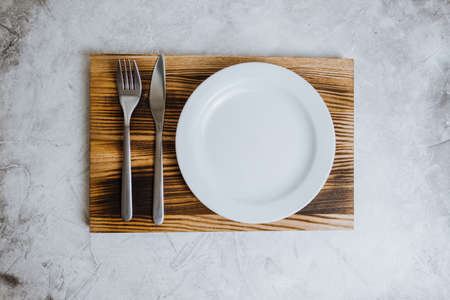 Empty white plate on a wooden board with cutlery on a gray background. High quality photo
