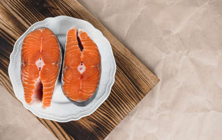 Fresh steaks of red salmon fish in a white plate on a wooden board with copy space. High quality photoの写真素材